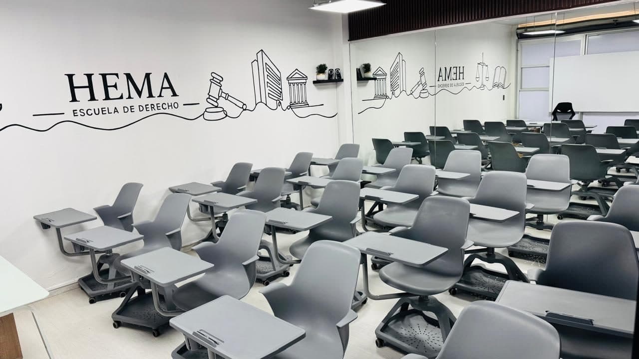 Aula del Instituto HEMA: el mural de línea continua con el rótulo «HEMA · Escuela de Derecho», un mazo de juez y edificios de justicia recorre la pared, con las butacas de paleta sobre ruedas dispuestas en filas.